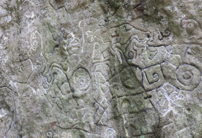 Indigenous shapes and artwork carved into a mossy stone wall in Panama.