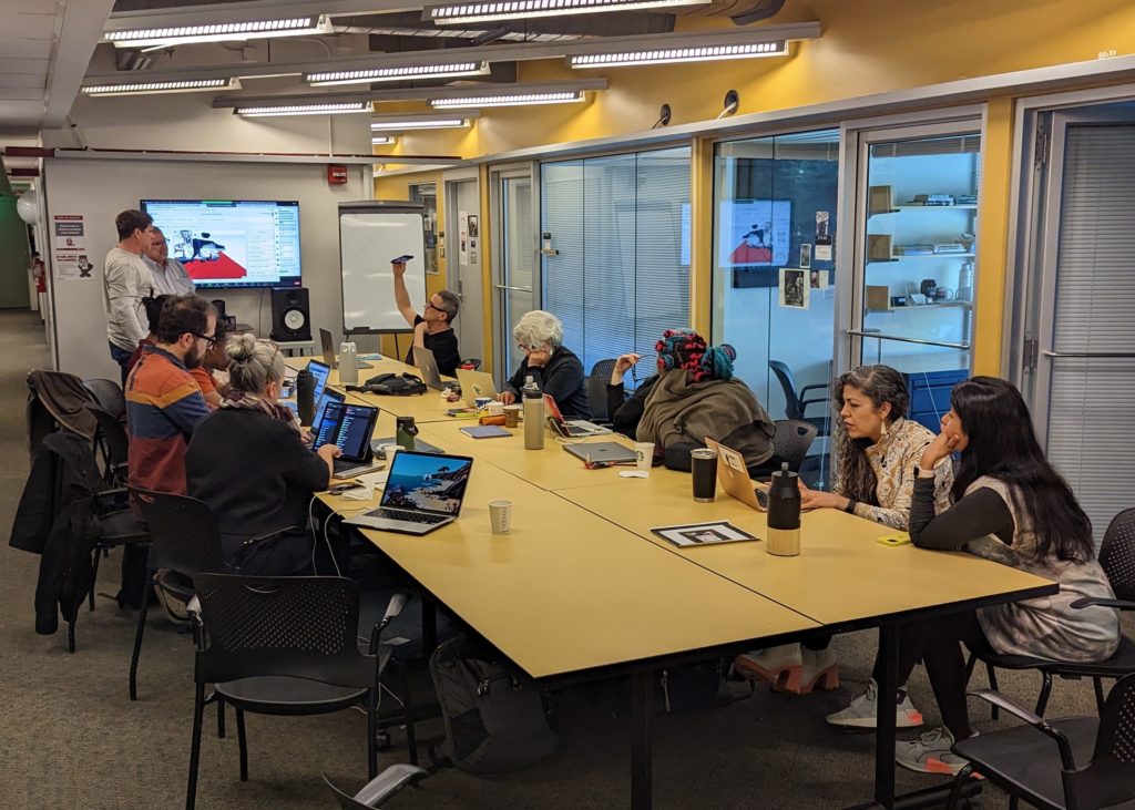 Tho ODL community seated at a long conference table for a workshop. People are working on phones and laptops to create their own AR experiences.