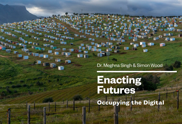 A wide photo of many small white houses on a green hill. Behind the hill is a mountain and some dark clouds. Text on the image says "Dr. Meghna Singh & Simon Wood" "Enacting Futures" "Occupying the Digital" on three separate lines.